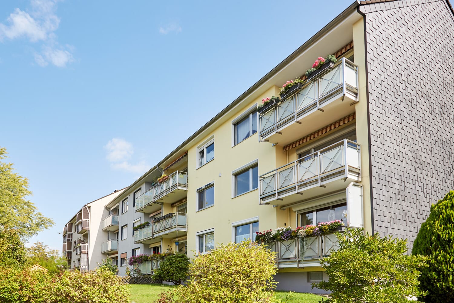 Wohnhaus mit begruenten Balkonen unter blauem Himmel
